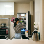 Woman wiping down refrigerator shelves with eco-friendly cleaner no off needed.