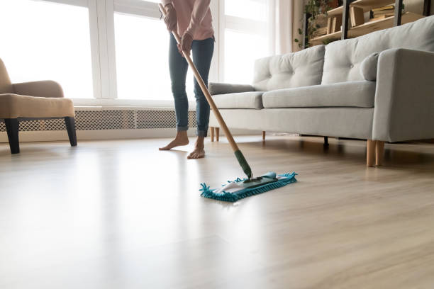 Person mopping hardwood floor in bright living room, showcasing an easy cleaning habit for a spotless home.