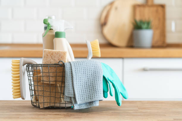 Cleaning supplies, including brushes, sponges, and gloves, neatly organized in a wire basket on a tidy kitchen counter.